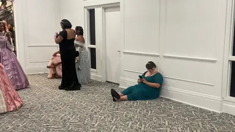 @moreofnita Women dressed in their finest clothes, sitting on the floor and scrolling through their phones