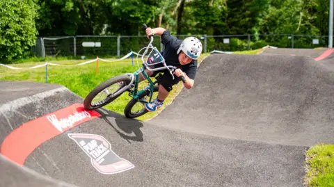 Pete Scullion A young rider in black with a white helmet on goes round a bend on the track