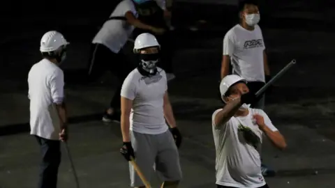 Reuters Men in white T-shirts with poles are seen in Yuen Long after attacked anti-extradition bill demonstrators at a train station, in Hong Kong