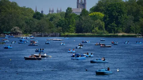 PA Media People ride pedalos on the Serpentine in Hyde Park, London, in view of the Palace of Westminster on Bank Holiday Monday