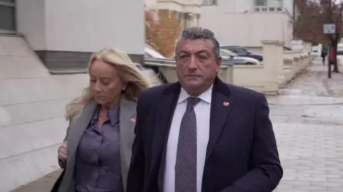 Dawid Wojtowicz Man in suit with woman in grey jacket walk down street