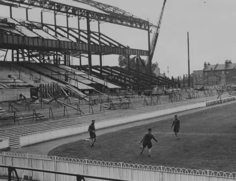 Fox Photos Tottenham Hotspur players Walter Alsford, Michelles and George Greenfield training on the pitch at White Hart Lane in front of where the new East Stand is being built, 26th July 1934