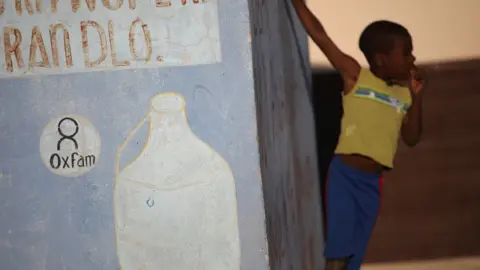 Reuters Boy stands next to Oxfam sign