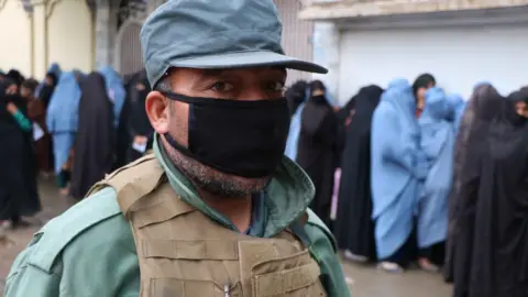 EPA Security force stands guard as women line up to receive free ration distributed by WFP