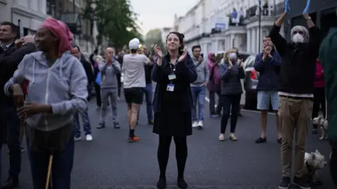 PA Media People gather on the street to clap for the NHS