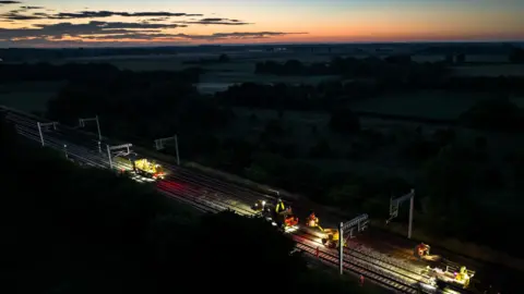 Network Rail Work taking place overnight on rail lines. Machines can be seen on the track. In the background the sun is setting over the horizon