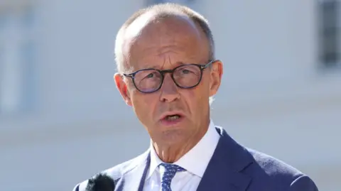 EPA Friedrich Merz speaks wearing a blue suit to journalists on 25 August 2026
