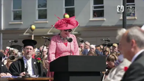 The Government of Jersey St Martin Constable Karen Shenton Stone giving a speech in Liberation Square in Jersey. She is stood at a podium.