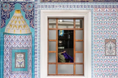 Robert Ciuccio / AFP A Muslim woman arranges her veil at the Nizamiye Mosque. Outside, the building is decorated in floral blue and purple tiles.