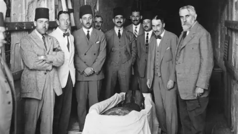 Griffith Institute/Harry Burton A group of English and Egyptian experts crowded around the mummy of Tutankhamun.