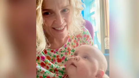 Georgina Jones A selfie of Georgina Jones holding her son Osian. Osian is looking up at her and has a tube going into his nose. Ms Jones is smiling looking at the camera. She is wearing a floral top.