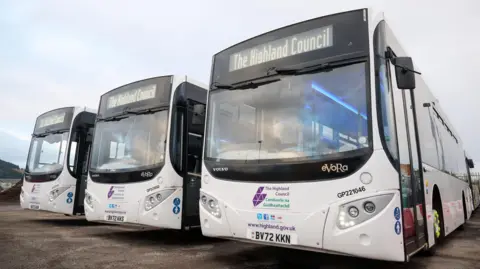 Three white buses parked next to each other. The windows are large and outlined in black. Highland Council's name and logo are printed on the front.