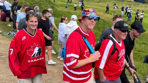 Três pessoas vestindo uma camisa canadense vermelha. Eles estão de pé no campo aberto no retrato real com uma multidão de pessoas em segundo plano. 