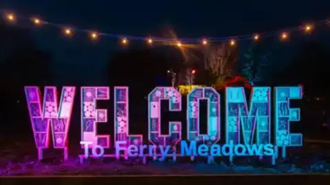 Nene Park Trust A sign that reads "Welcome to Ferry Meadows" is lit up in pink and blue. 