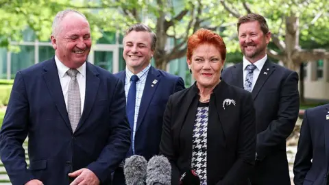 Getty A group of four men and a woman in suits smile with trees in the background.