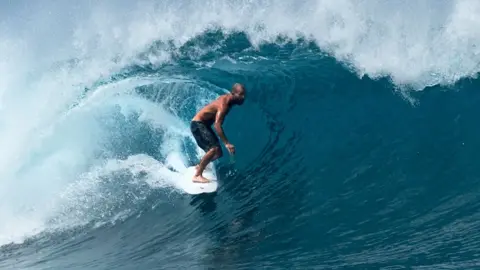 Getty Images A surfer surfs though a tube formed by a large wave in the sea off the Mentawai islands