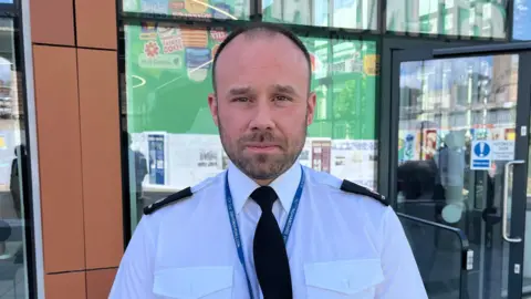 City centre commander of Nottinghamshire Police Superintendent Chris Pearson. A white, balding man with black hair wearing police uniform - a white shirt and black tie. He is standing outside Nottingham Central Library in Nottingham City Centre. 