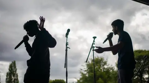 A shadow of two young men performing with microphones on a stage