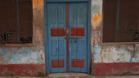 Adeeb Anwar/BBC A blue and red door which is the entrance to Mohammad Akhlaq's house