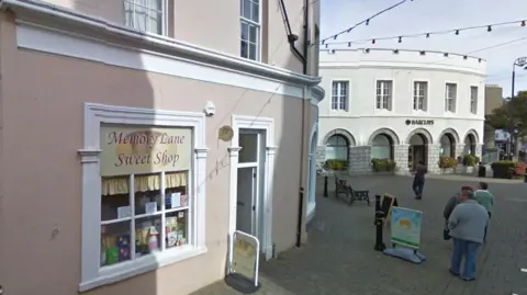 Google The exterior of Memory Lane Sweet Shop, a terra-cotta building, you can see the square in the background.