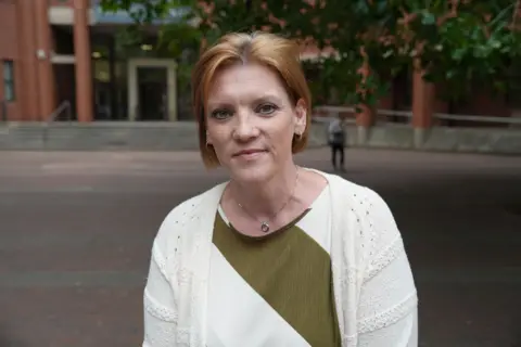 Natalie Smith standing outside Hull Crown Court. She has short red hair and is wearing a white and dark green top with a white cardigan.