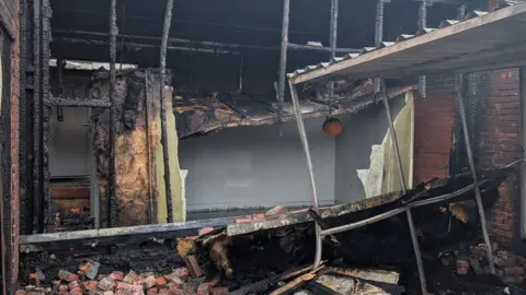 Supplied A burnt out building, with collapsed bricks and burnt pieces of wood. Part of the structure has fallen down. 