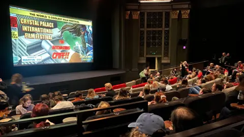 Crystal Palace's Everyman cinema shows rows of cinemagoers looking at a CPIFF poster with the words 'the astonishing CPIFF'