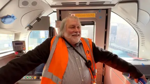 An engineer in hiviz stands in the driver cab