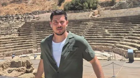Sussex Police Valera Sharavara is standing behind a railing at an outdoor amphitheatre with tiered stone seating and dry hillside in the background.