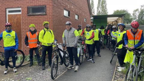 Men and women smiling with their bikes in hi-vis jackets