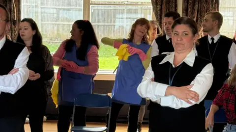 WAOS A group of actors dressed in prison garb in a rehearsal hall.
