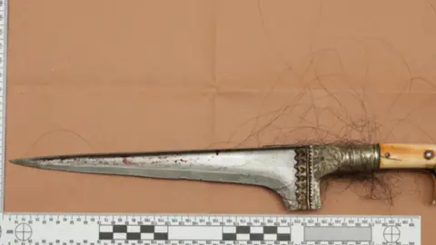 Crown Prosecution Service A long knife next to a ruler for reference with dark hair attached to the handle 