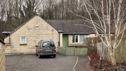Newton House in Bath which is a small care home. It is a bungalow with a green picket fence with a disability van parked outside.