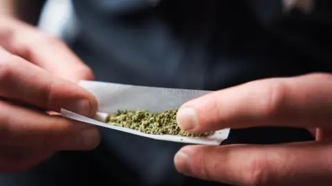 An anonymous man wearing a dark t-shirt rolls a marijuana cigarette in this stock photo. 
