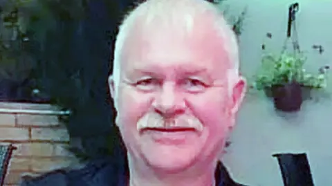 Police Scotland Bill Ireland headshot style picture. He is smiling at the camera. He has short grey hair and a grey moustache. 