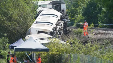Eddie Mitchell Workers in hi vis jackets inspecting a derailed train.