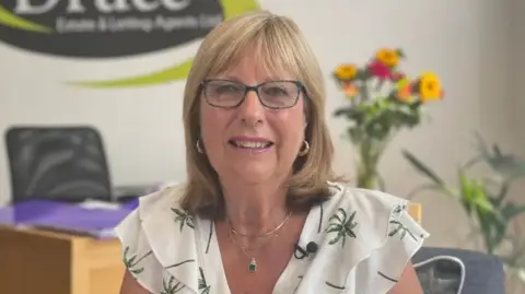 Zoie O'Brien/BBC Linda Druce from Druce Estate & Letting Agents sitting in her office smiling into the camera 