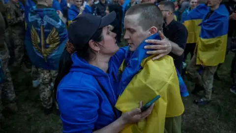 A Ukrainian prisoner of war wrapped with the national flag embraces his mother as he returns after a prisoner swap with Russia in Ukraine, 19 April 2025.