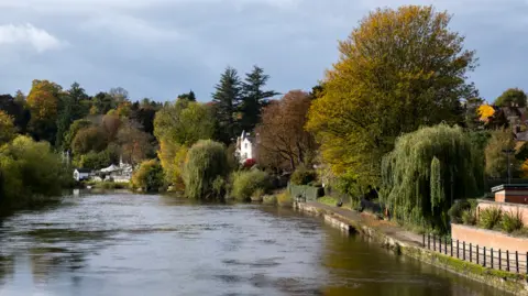 A wide river with trees along both sides and a footpath seen on the right hand side