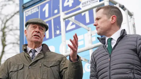 Nigel Farage and Robert Jenrick speaking at a news conference at a petrol station in Derbyshire