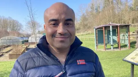 BBC/Cathy Minton Bald man in a navy blue puffa jacket standing outside a city farm