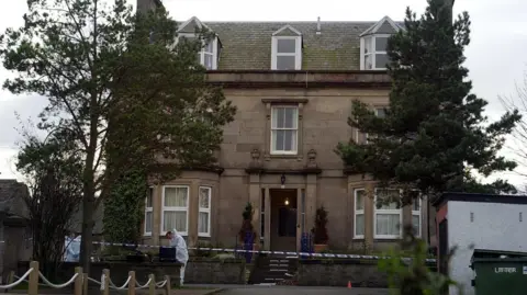 PA Media Exterior of the Wilson family home, scene of the murder, with forensic officers wearing white and police caution tape around the property