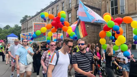 Pride marchers in Glasgow carrying rainbow-coloured balloons and flags 
