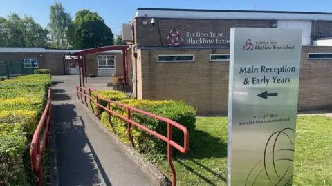 Blacklow Brow School A view of a brick school building with a metal sign reading 'Blacklow Brow School Main Reception and Early Years' in black lettering. 