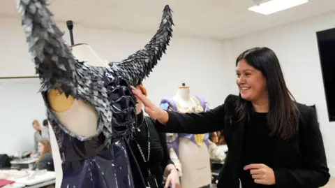 PA Media Culture Secretary Lisa Nandy, dressed all in black and smiling, inspects a fantasy-style costume with grey metallic horns on her visit to Pinewood Studios. 