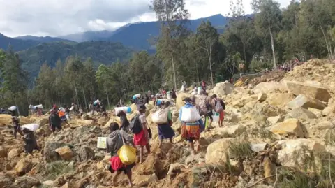 People carry bags on their backs as they walk through terrain covered by boulders in Enga province, Papua New Guinea