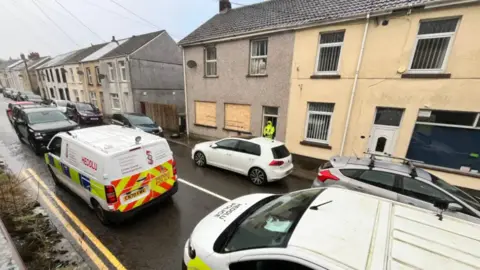 Residential street with terraced houses with cars parked and police van 