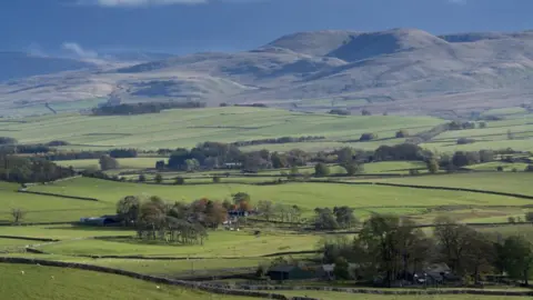 Getty Images The view from Orton Scar in Cumbria, looking towards the Howgill Fells. The hills are green and scattered with trees and farm buildings.