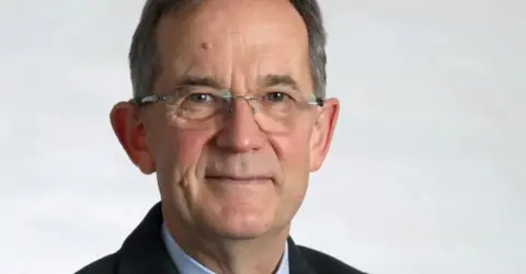 Goverment of Jersey Man wearing glasses in front of an off-white background