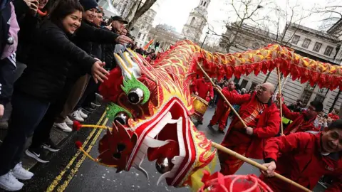 Getty Images A red paper dragon being paraded on wooden poles passes by a group of spectators on a London street. 